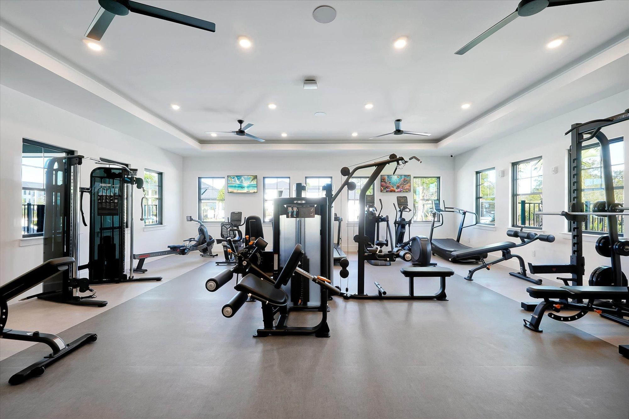 Bright gym with various exercise machines, weight equipment, and large windows letting in natural light.
